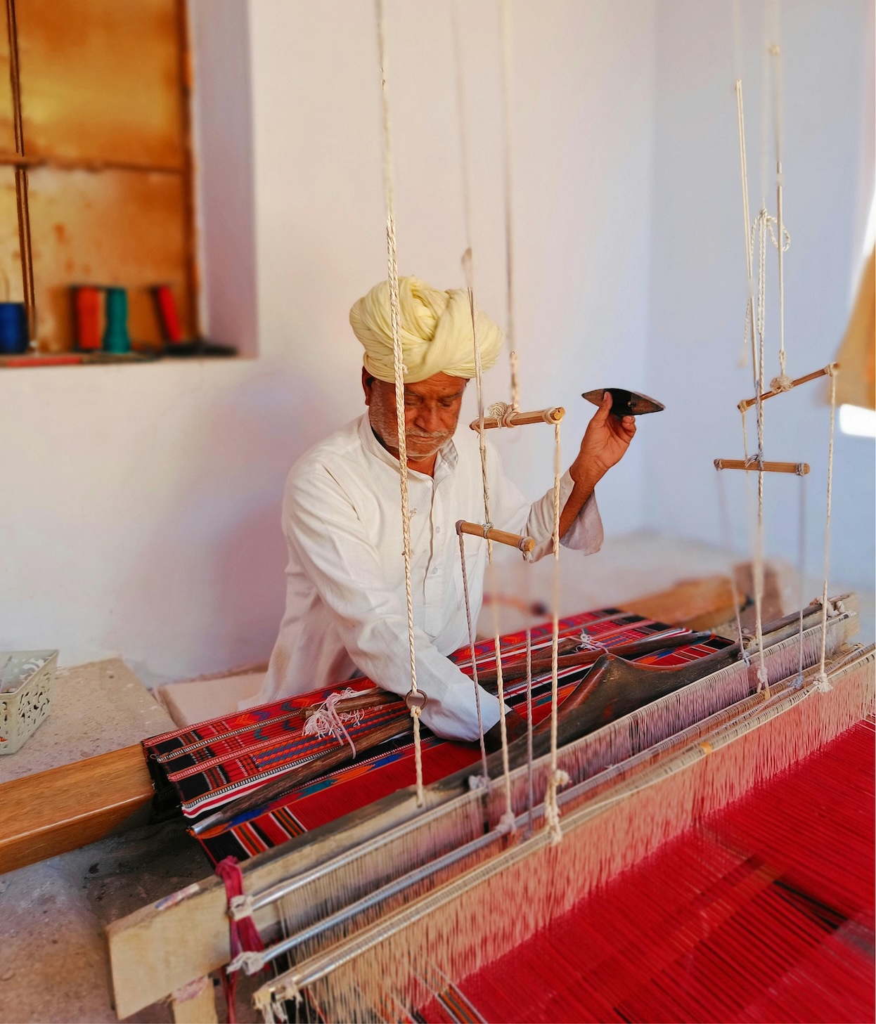 Artisan weaving a red textile on a loom